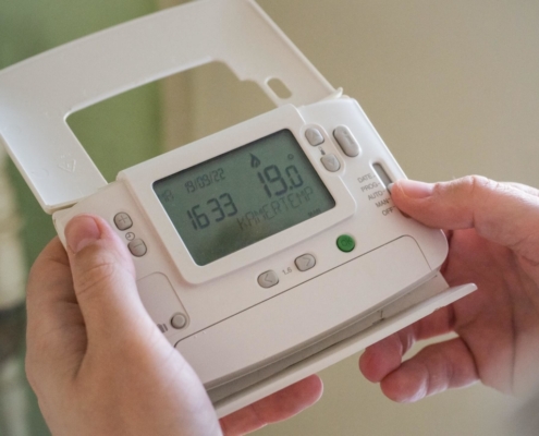 A person holding their thermostat control examining it for any HVAC myths.